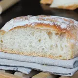Pane fatto in casa, con crosta dorata e mollica alveolata, adagiato su un tovagliolo di lino.