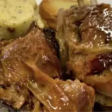 Succulento agnello al forno, dorato e lucido, servito con patate arrosto e una crema verde.