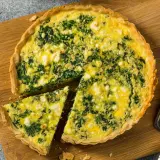 Torta salata ricotta e spinaci dorata e invitante, con una fetta tagliata su un tagliere di legno.