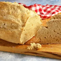 Pane casereccio con lievito istantaneo, tagliato su un tagliere di legno, con un tovagliolo a quadri rossi e bianchi.
