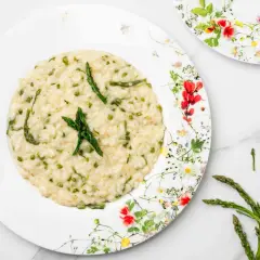 Un cremoso risotto con asparagi selvatici, guarnito con punte di asparago fresco su un piatto fiorito.