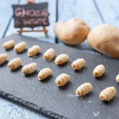 Gnocchi fatti in casa, morbidi e rigati, pronti per essere cucinati. Due patate sullo sfondo, ingredienti freschi per un piatto delizioso.