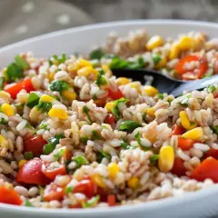 Insalata di farro colorata con pomodorini, mais e prezzemolo fresco, servita in una ciotola bianca con un cucchiaio nero.