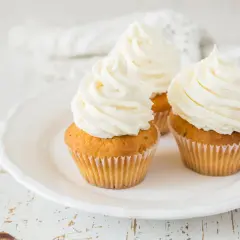Tre cupcake su un piatto bianco, con abbondante crema al burro soffice e ariosa.