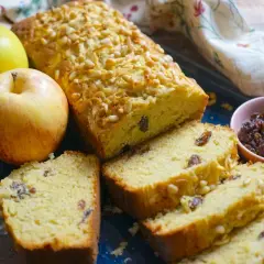 Plumcake alle mele soffice e profumato, con uvetta e pinoli, accompagnato da mele fresche e una ciotolina di uvetta.