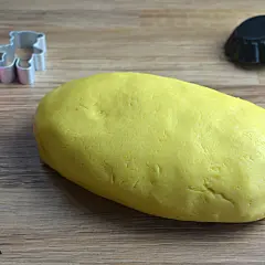 Yellow pasta frolla dough with cookie cutters and tart molds on a wooden surface.
