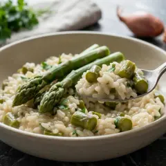 Un cremoso risotto con asparagi freschi, guarnito con prezzemolo tritato. Una forchettata mostra la consistenza perfetta.