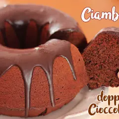Ciambella al cioccolato, soffice e golosa, con una glassa lucida che cola. Una fetta viene sollevata, mostrando la sua consistenza.