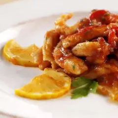 Straccetti di pollo al limone succulenti, conditi con salsa rossa e guarniti con fette di limone e prezzemolo fresco.