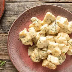 Bocconcini di pollo al latte cremoso, conditi con erbe aromatiche, serviti su un piatto rustico.