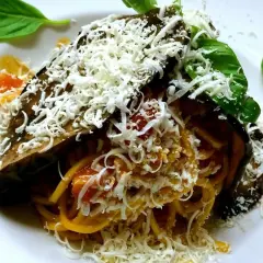Pasta alla Norma ricetta: spaghetti con melanzane fritte, pomodoro e ricotta salata grattugiata, guarnita con basilico fresco.