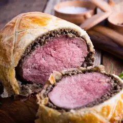 Un succulento filetto alla Wellington, tagliato a metà, rivela la sua carne rosa e tenera, avvolta in pasta sfoglia dorata e funghi.