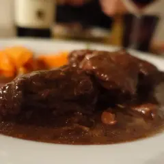 Un succulento brasato al barolo, tenero e profumato, accompagnato da carote arancioni su un piatto bianco.