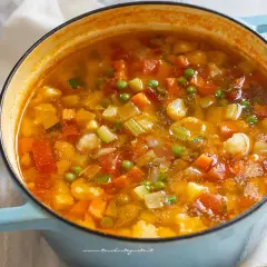 A close-up of a light blue pot filled with steaming minestrone soup, showing chunks of vegetables.