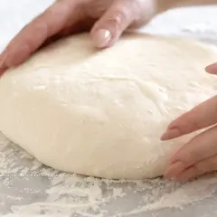 Mani che lavorano un impasto soffice, pronto per diventare una pizza giallo zafferano.