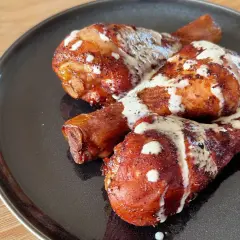 Tre succulenti fusi di pollo arrostiti, conditi con spezie e nappati con una cremosa salsa bianca, serviti su un piatto scuro.