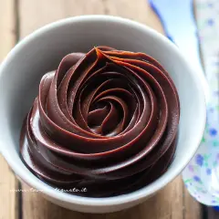 Una ciotola bianca piena di ganache al cioccolato, con un vortice perfetto. Vicino, cucchiai colorati.