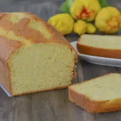 Plumcake al limone soffice e profumato, con una fetta tagliata e pronta da gustare. Sullo sfondo, limoni freschi.