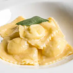 Ravioli dorati in salsa cremosa, guarniti con una foglia di salvia. Il ripieno per ravioli è un segreto gustoso.