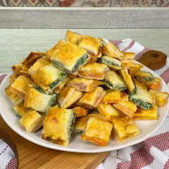 Un mucchio di salatini con pasta sfoglia, alcuni ripieni di spinaci e altri di prosciutto, pronti per essere gustati.