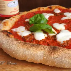 Pizza margherita con pomodoro, mozzarella filante e basilico fresco. La crosta dorata e alveolata è il risultato di una lunga lievitazione.