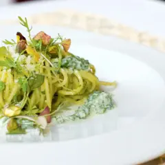 Spaghetti conditi con un cremoso pesto di pistacchi, guarniti con pistacchi interi e erbe fresche.