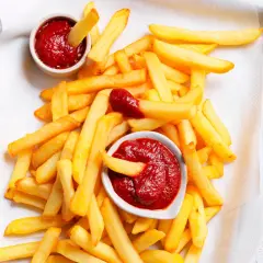 Patatine fritte dorate e croccanti con due ciotoline di ketchup fatto in casa, una con una patatina che si tuffa dentro.