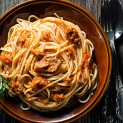Un piatto di spaghetti al tonno, conditi con un sugo saporito e guarniti con un rametto di rosmarino, pronti per essere gustati.