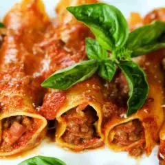 Cannelloni di carne ricetta della nonna, ripieni di ragù e conditi con sugo rosso e basilico fresco.