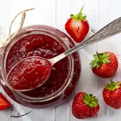 Un vasetto di marmellata di fragole fatto in casa, con fragole fresche e un cucchiaio pieno di dolcezza rossa.