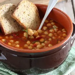 Una ciotola di terracotta con zuppa di ceci, pomodoro e rosmarino, accompagnata da fette di pane rustico.