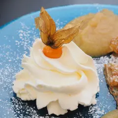 Panna montata soffice con physalis, su un piatto blu cosparso di zucchero a velo, accanto a un dolce che ricorda il pan di spagna.