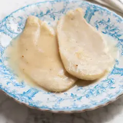 Due scaloppine al vino bianco, tenere e succulente, servite su un piatto di ceramica decorato con motivi blu.