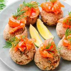 Polpette di pesce dorate, guarnite con salmone affumicato, aneto e spicchi di lime. Un antipasto raffinato e gustoso.