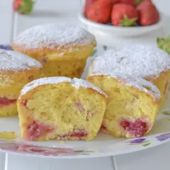 Morbidi muffin alle fragole, cosparsi di zucchero a velo, invitano a un dolce assaggio. Pezzi di fragola succosa si intravedono nell'impasto soffice.