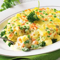 Insalata russa ricetta della nonna: un piatto cremoso con patate, carote, piselli e uova, guarnito con prezzemolo fresco.