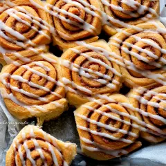 A close-up shot of freshly baked cinnamon rolls drizzled with white icing.