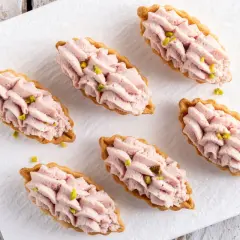 Piccoli cestini di pasta brisée ricetta, ripieni di crema rosa e guarniti con pistacchi.