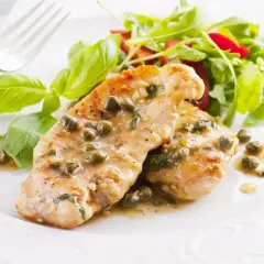 Deliziose scaloppine di pollo al limone e capperi, servite con un'insalata fresca e foglie di basilico.