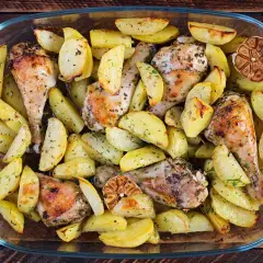 Un succulento pollo e patate al forno, dorati e profumati, in una teglia di vetro.