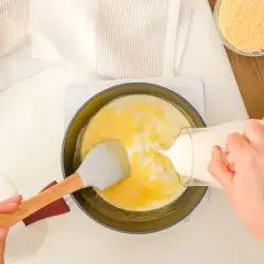 Mani versano latte in una padella con uova e formaggio grattugiato, preparando una deliziosa crema di parmigiano.