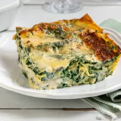 Una fetta di lasagne ricotta e spinaci, dorata al forno, su un piatto bianco.