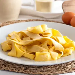 Piatto di pasta fresca fatta in casa, con uova e farina sullo sfondo.