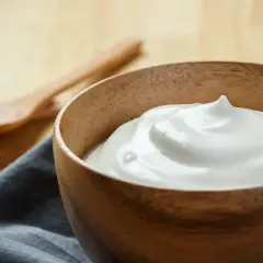 Una ciotola di legno contiene una soffice crema al latte, pronta per essere gustata. Due cucchiai di legno sono sullo sfondo.