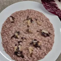 Un cremoso risotto al radicchio rosso, con pezzetti di verdura che spuntano. Accanto, una foglia di radicchio fresco.