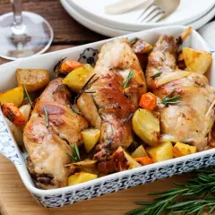 Coniglio al forno dorato con patate e carote, profumato al rosmarino, servito in una pirofila decorata.