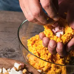 Mani che preparano polpette di riso con cubetti di prosciutto e formaggio.