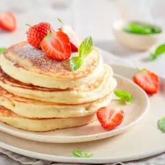 Pancake allo yogurt soffici e dorati, guarniti con fragole fresche e zucchero a velo. Un dolce inizio di giornata.