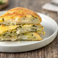 Fette di torta salata con zucchine e formaggio, impilate su un piatto bianco.