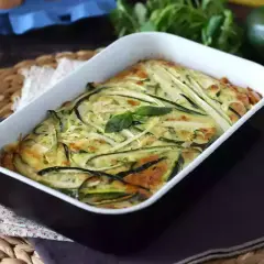 Deliziosa frittata di zucchine al forno, dorata e profumata, guarnita con basilico fresco.